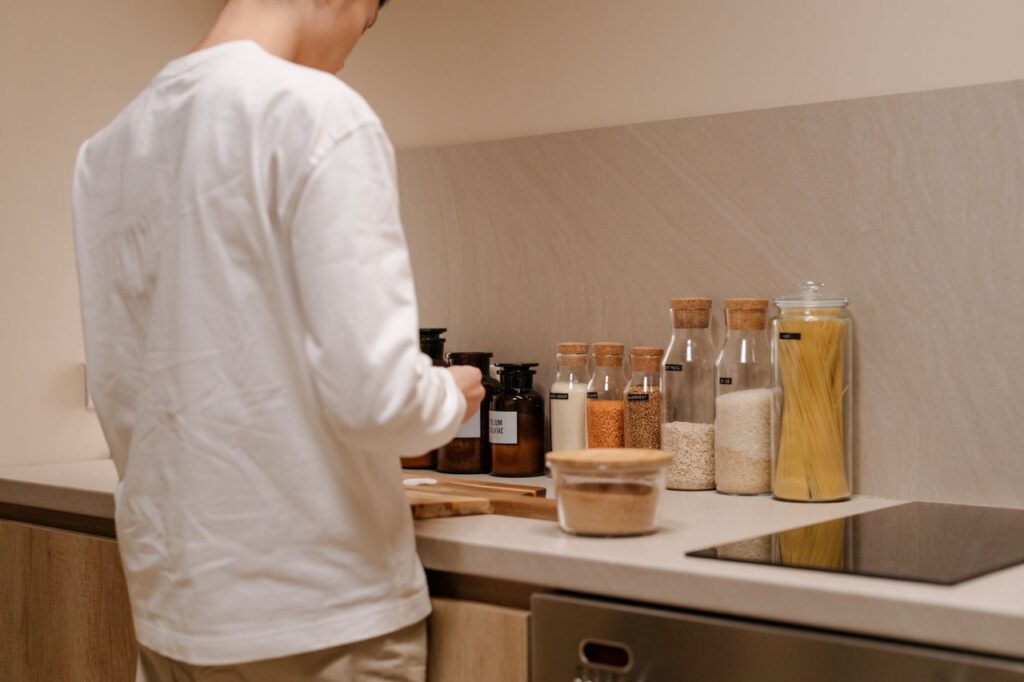 Man in white shirt in a kitchen with jars and spices, focusing on organization and design.